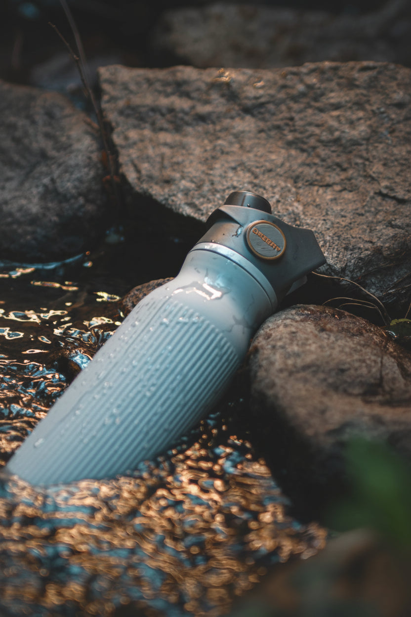 OASSAY water filtration bottle in natural water source.